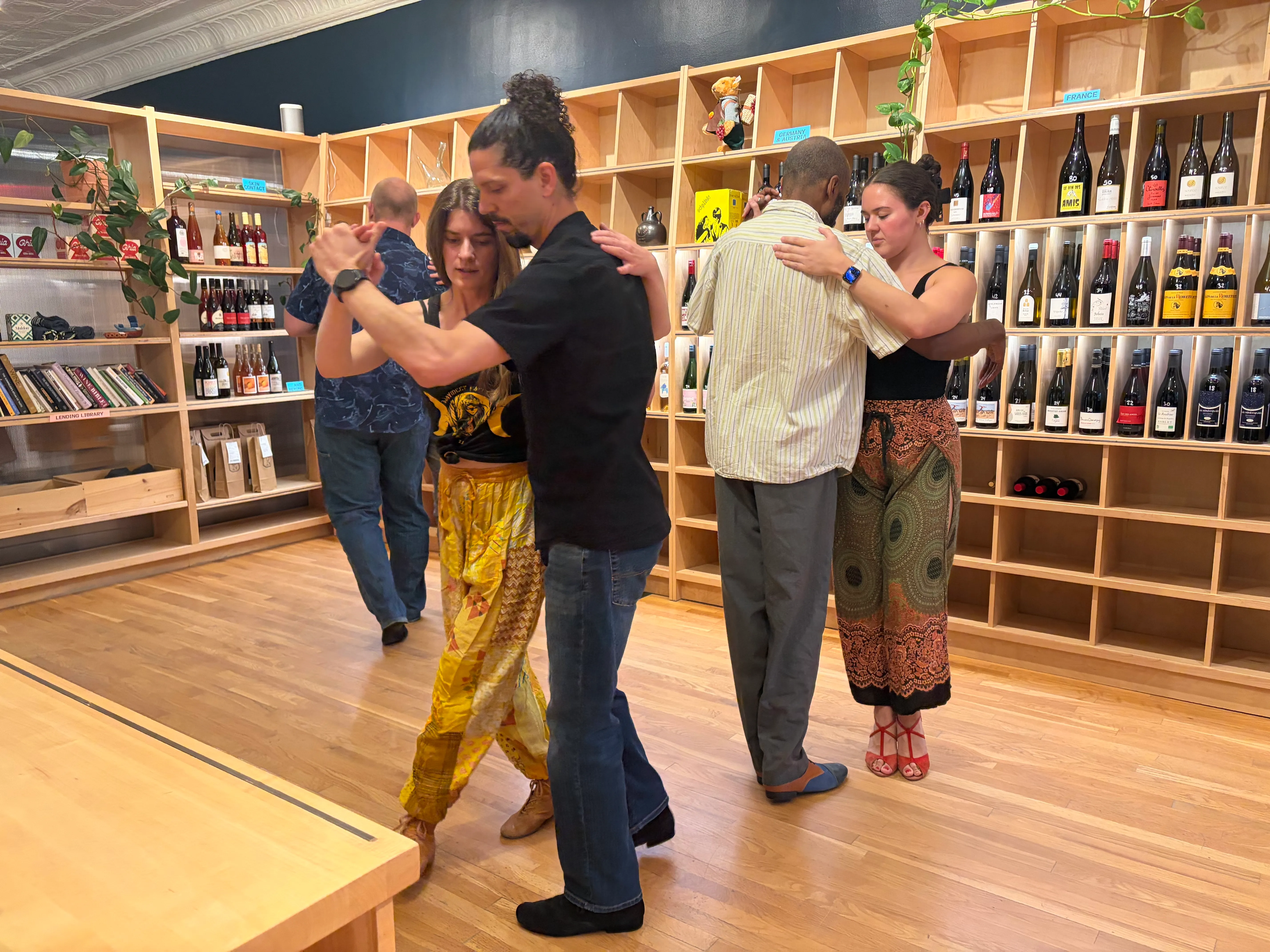 Couples practicing tango in front of the wine shelves at Ritual Wines.